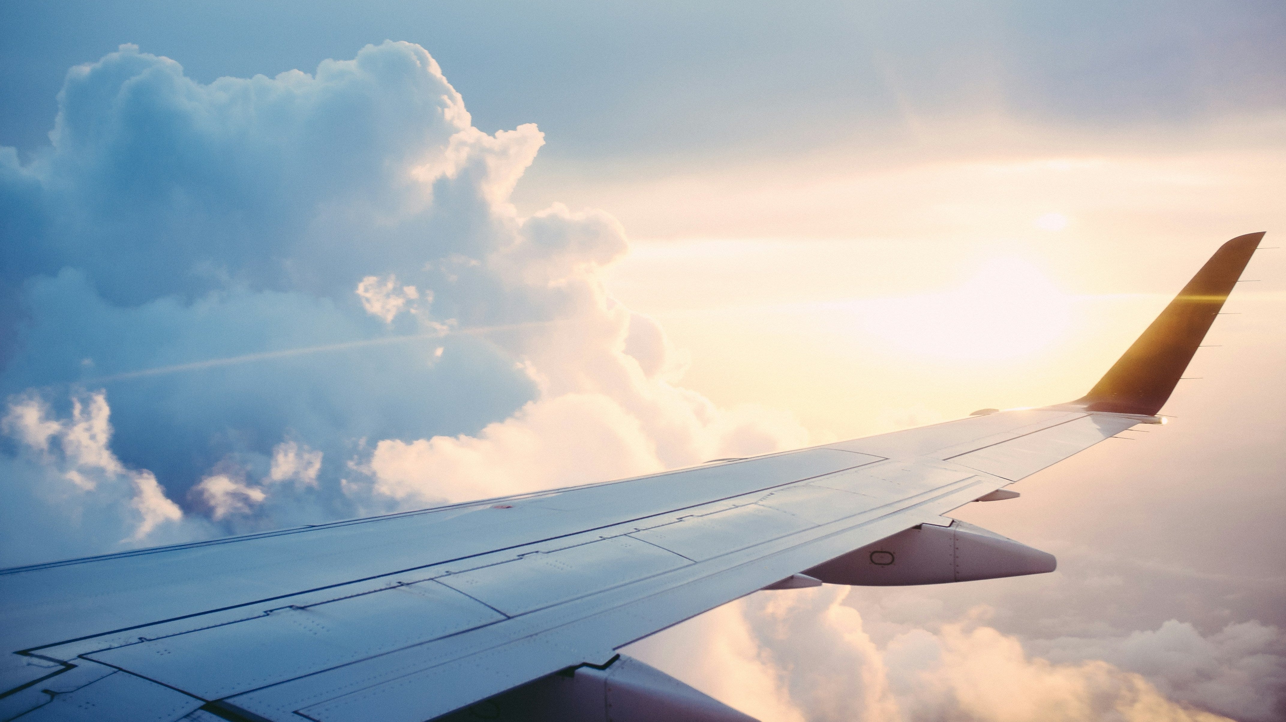 Image across the wing of a plane with the sun shining through clouds.