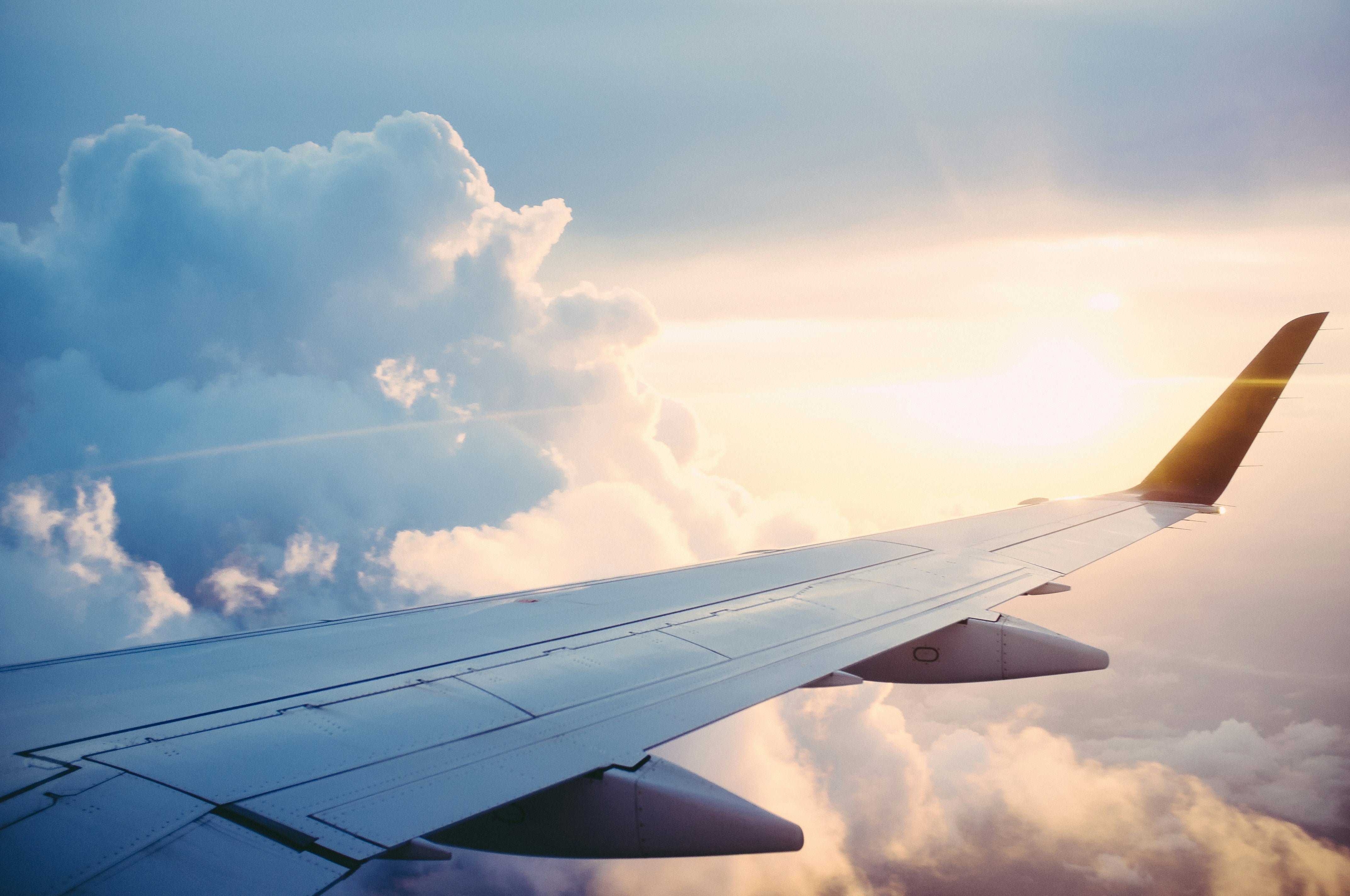 Image across the wing of a plane with the sun shining through clouds. 